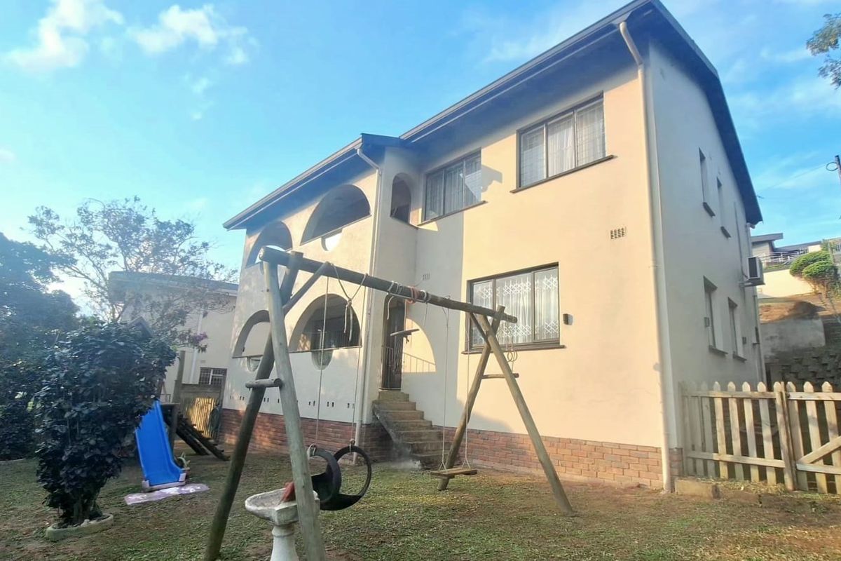 Rear view of a two-story residential house featuring arched balcony detailing, brick plinth, and a garden area.