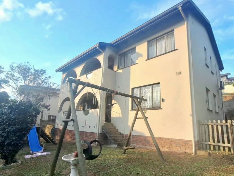 Rear view of a two-story residential house featuring arched balcony detailing, brick plinth, and a garden area.