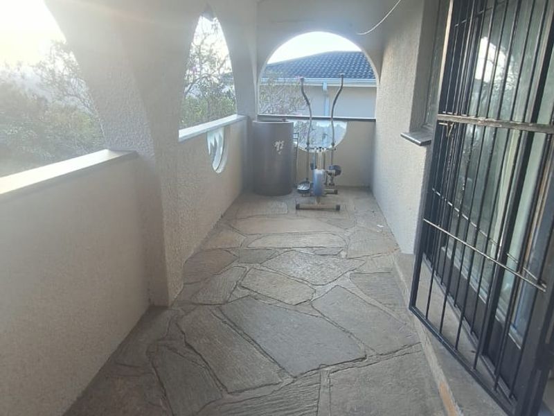 A covered balcony featuring stone paving and arched architectural details, providing an outdoor space with security gate access.