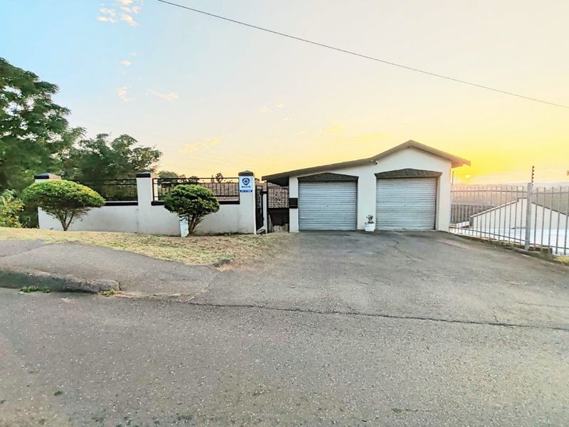 Front exterior view of the property featuring a double garage with roller shutter doors, paved driveway, and secure perimeter wall with electric fencing.