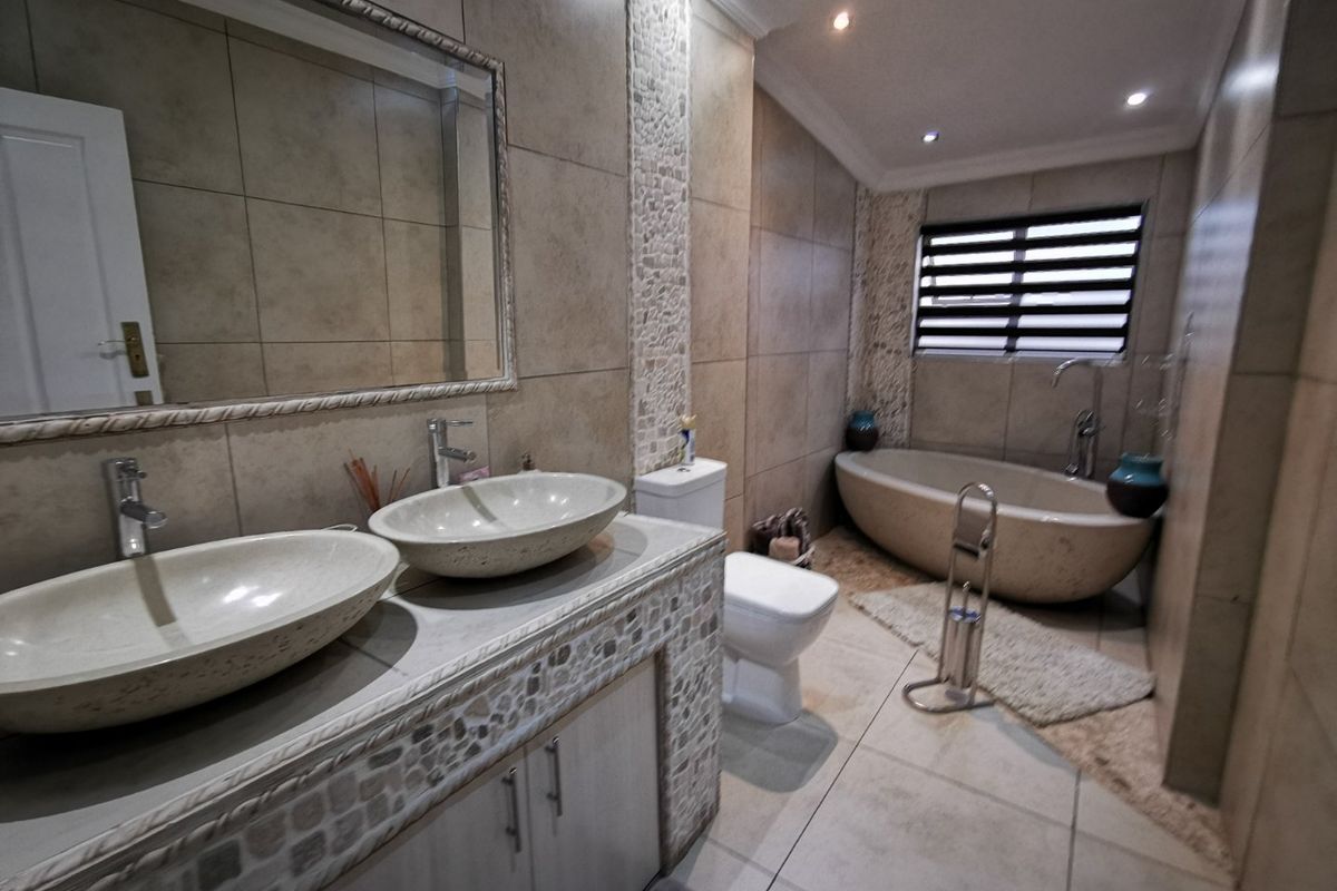 Modern bathroom featuring a double vanity with vessel sinks, a freestanding bathtub, and neutral stone-look tiling with decorative mosaic accents.