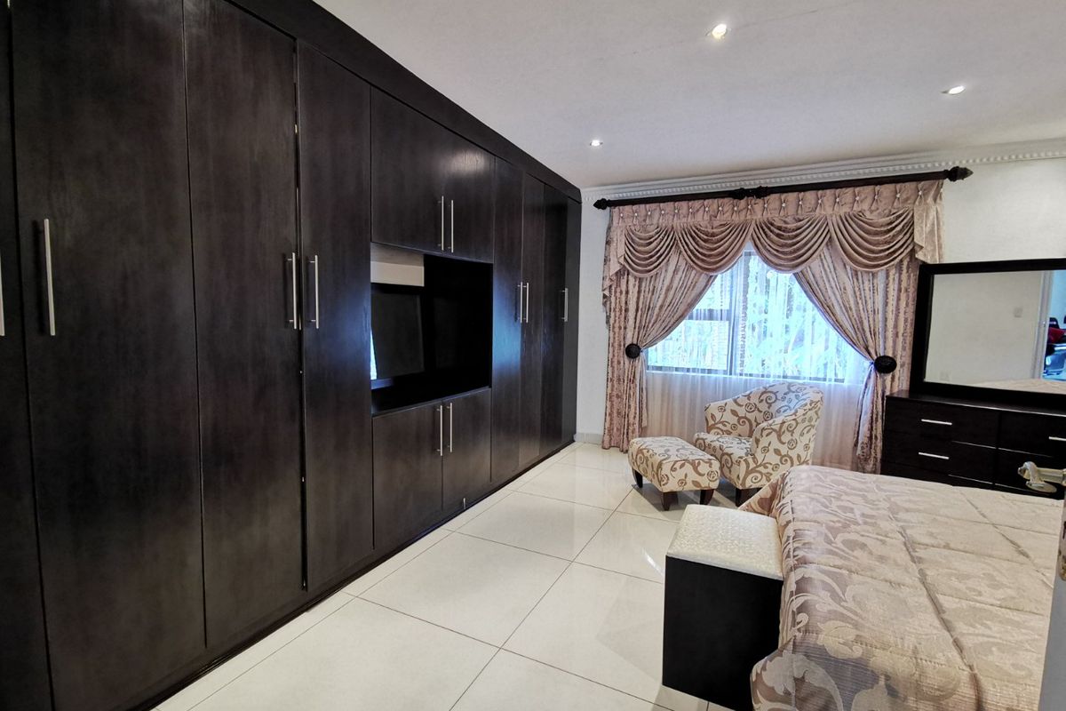 Spacious bedroom featuring extensive dark wood built-in cabinetry, large format floor tiles, and recessed ceiling lighting.