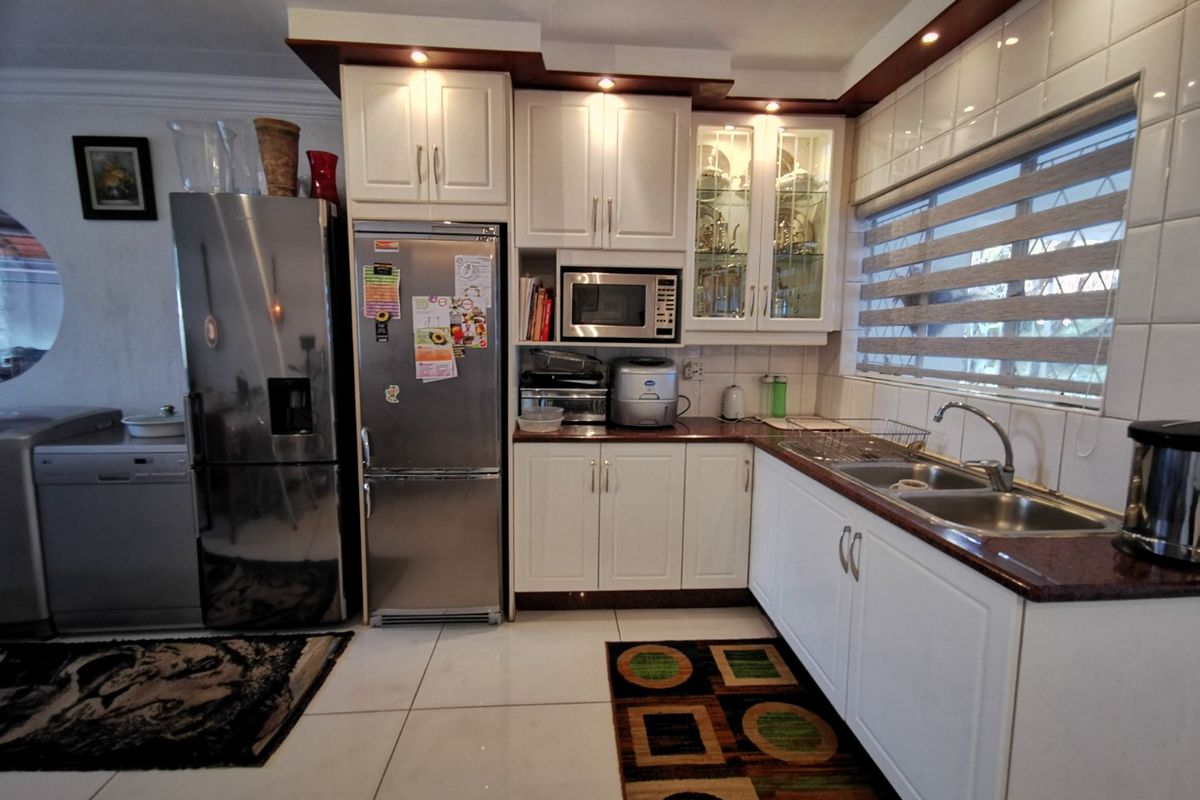 A functional kitchen featuring white cabinetry, granite countertops, a double basin sink, and built-in microwave, complemented by tiled backsplash and recessed lighting.