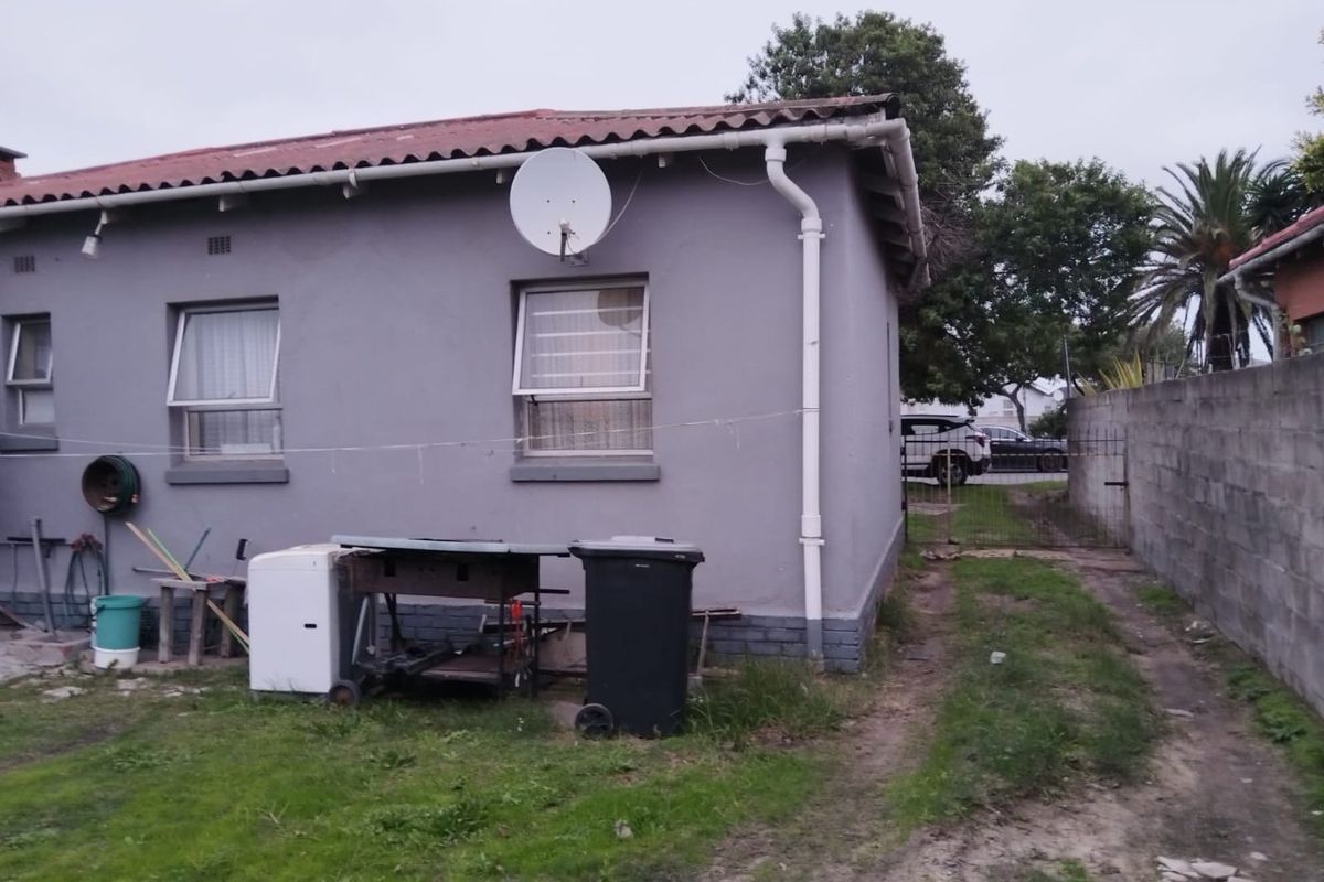 Rear exterior view of the house featuring a grey painted facade, gutter system, and a side access gate leading to the driveway.