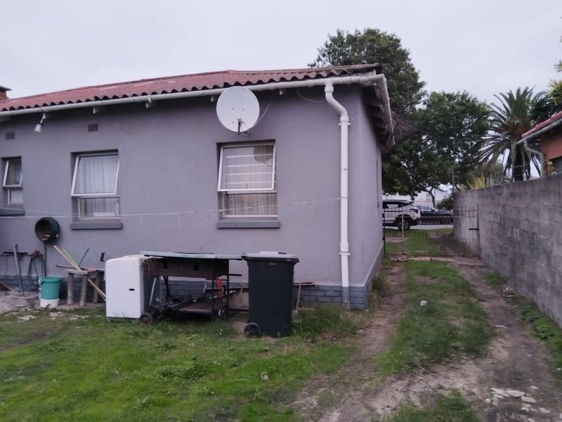 Rear exterior view of the house featuring a grey painted facade, gutter system, and a side access gate leading to the driveway.
