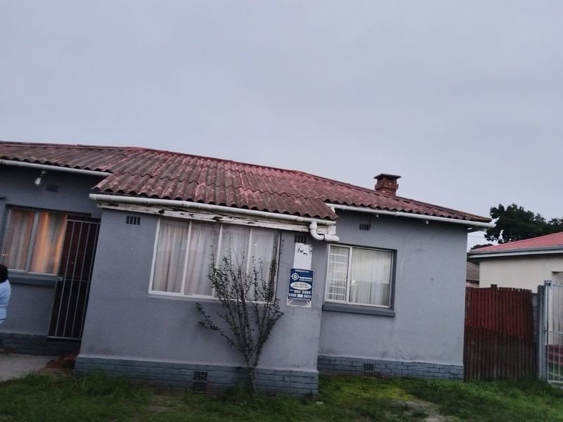Front elevation of a single-story house featuring a corrugated roof, brick chimney, and security gate entrance.