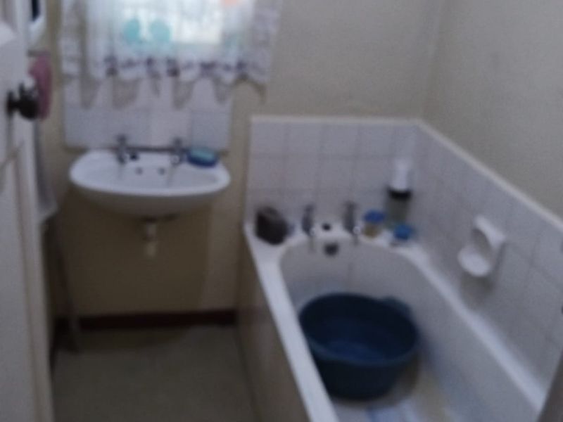 A dated bathroom featuring a wall-mounted basin and a built-in bathtub with tiled splashbacks, requiring modernization and cosmetic updates.