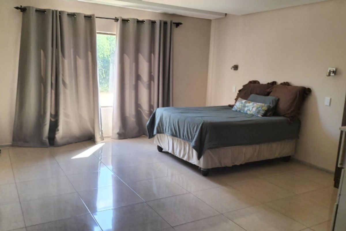 A spacious bedroom featuring neutral tiled flooring and large windows with curtain rails, providing a clean and functional living space.