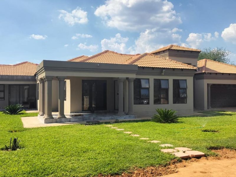 A well-maintained single-story residence featuring a covered patio with classical columns, terracotta roof tiles, and an attached garage set within a landscaped garden.