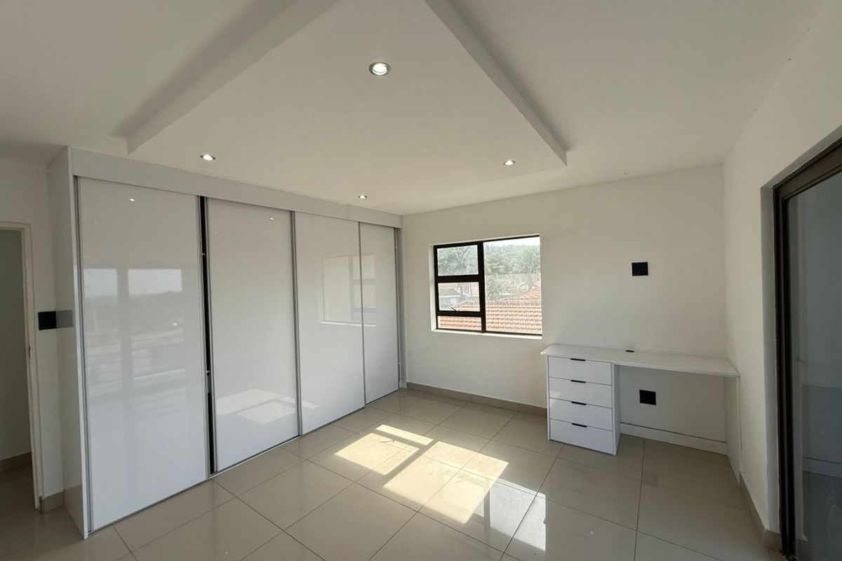 A bright, modern bedroom featuring high-gloss built-in cupboards, a built-in desk, tiled flooring, and a recessed ceiling with integrated downlights.