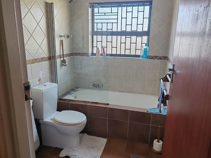 A functional bathroom featuring a built-in bathtub with a glass shower screen, tiled walls and flooring, and a standard toilet.