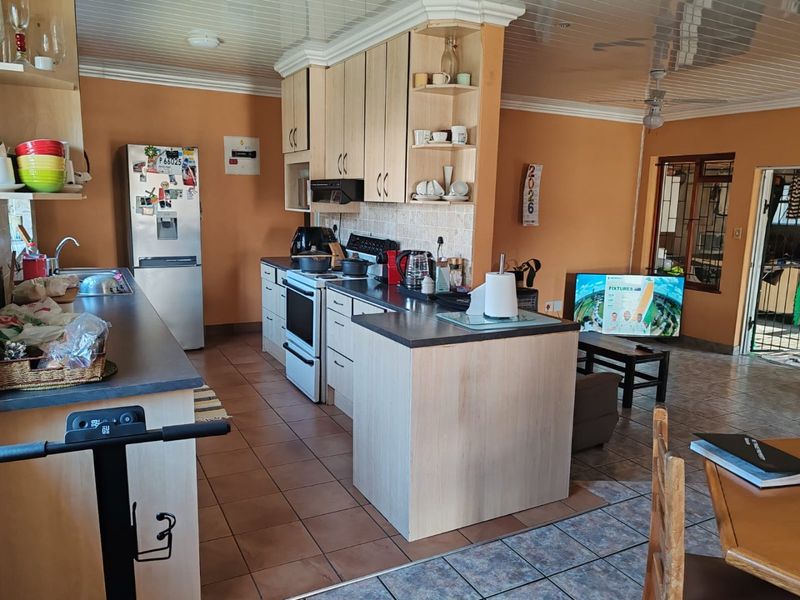 Open-plan kitchen and living area featuring light wood cabinetry, laminate countertops, tiled flooring, and direct access to an outdoor patio area.