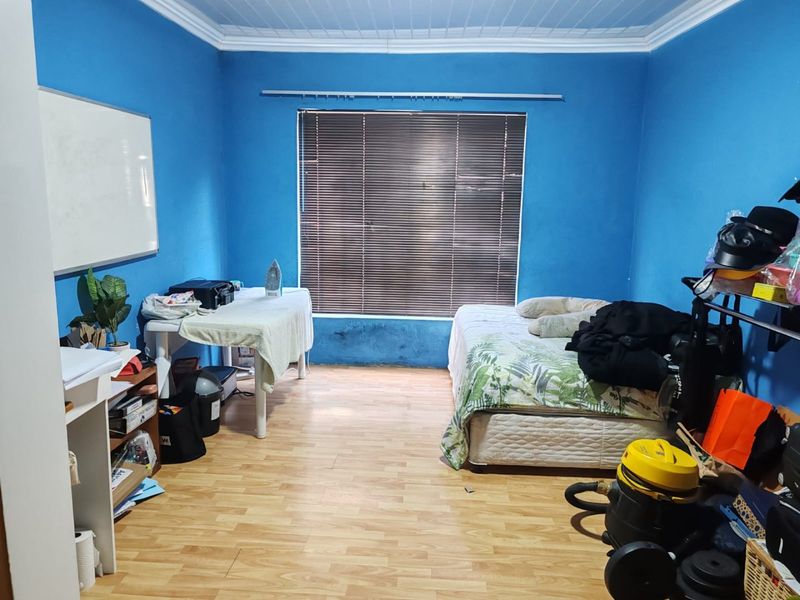 A bedroom featuring laminate flooring, coved ceilings, and venetian blinds, currently showing signs of wall damage and paint deterioration.