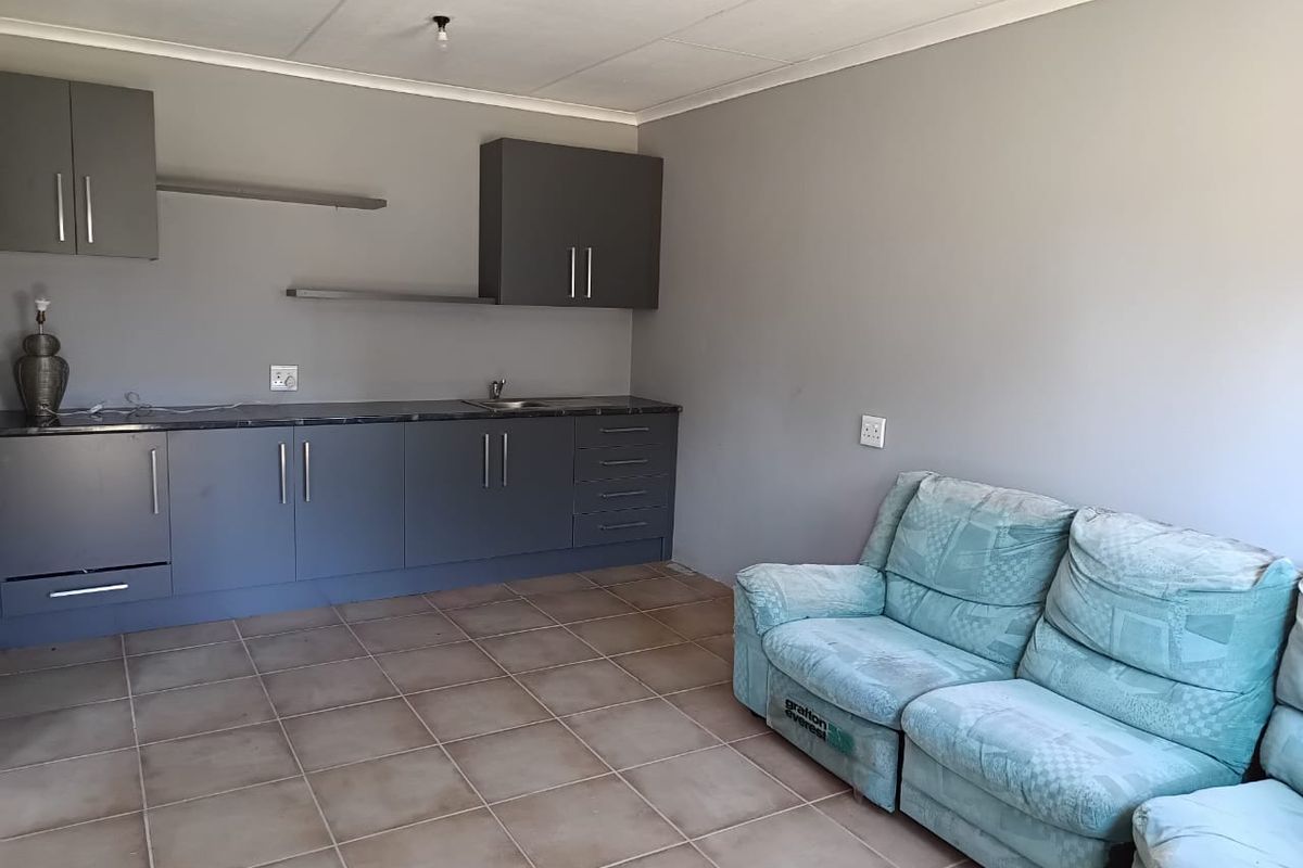 Open plan living area featuring a kitchenette with dark grey cabinetry, tiled flooring, and neutral wall finishes.