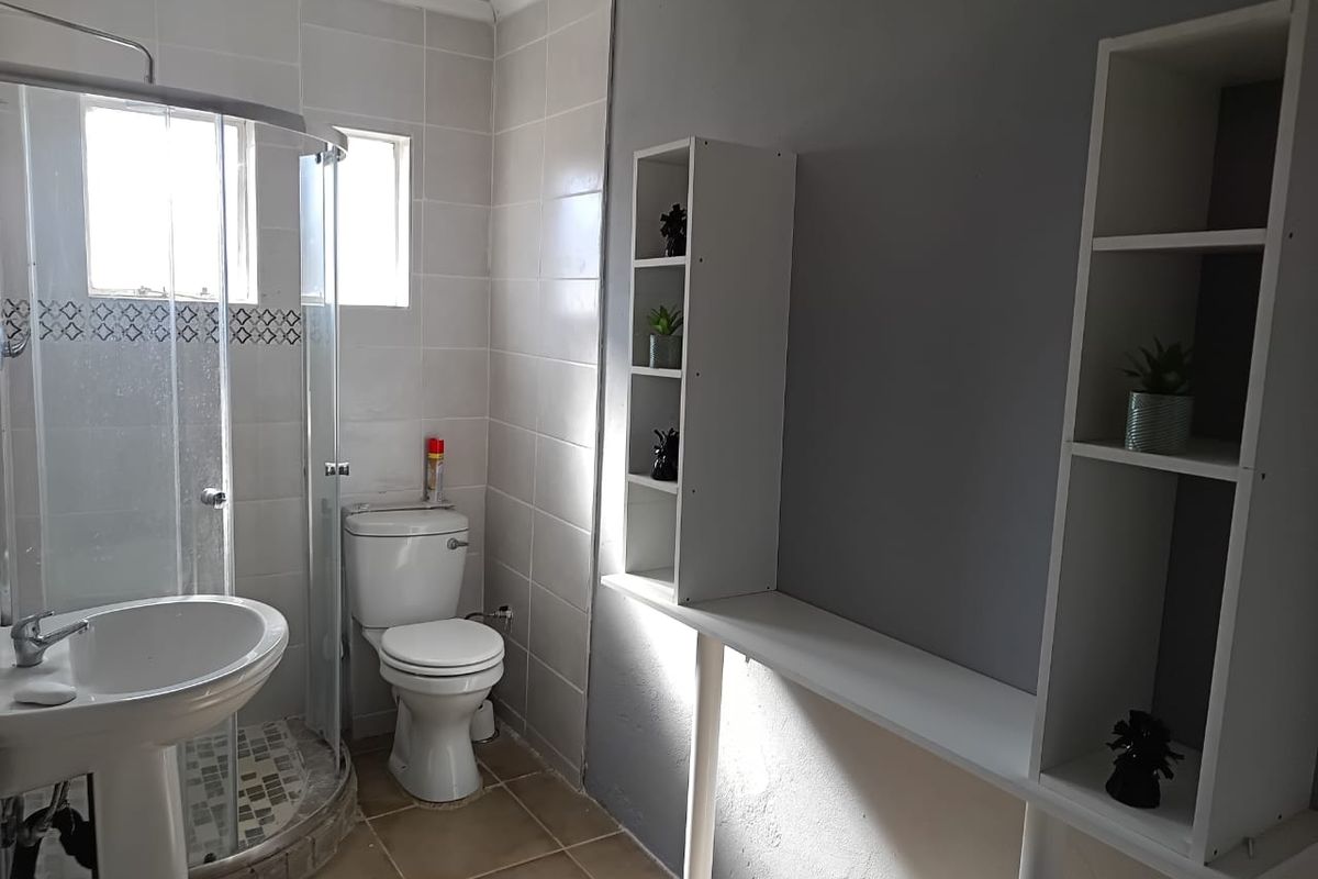A functional bathroom featuring a corner shower enclosure, pedestal basin, and toilet with neutral wall tiling and tiled flooring.