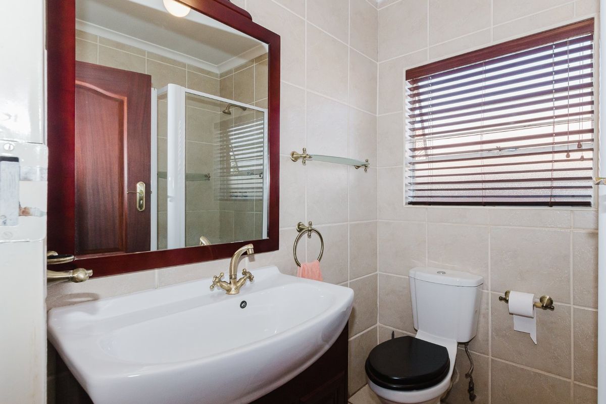 A functional bathroom featuring tiled walls and flooring, a pedestal basin with brass fixtures, a toilet, and a separate shower enclosure.
