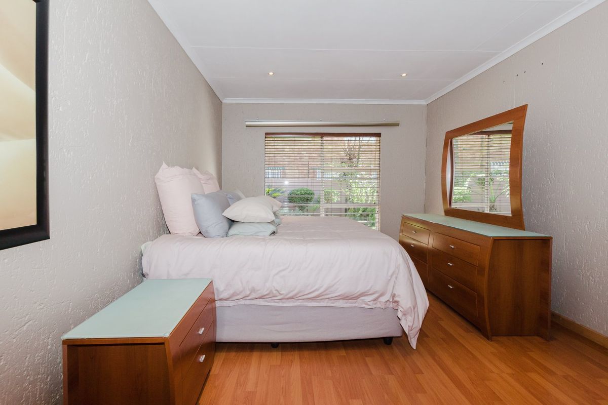 A well-maintained bedroom featuring laminate flooring, recessed downlighting, and venetian blinds, offering a clean and functional living space.