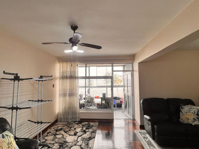 A living room featuring parquet flooring, a ceiling fan, and large windows providing natural light and access to an adjoining balcony.
