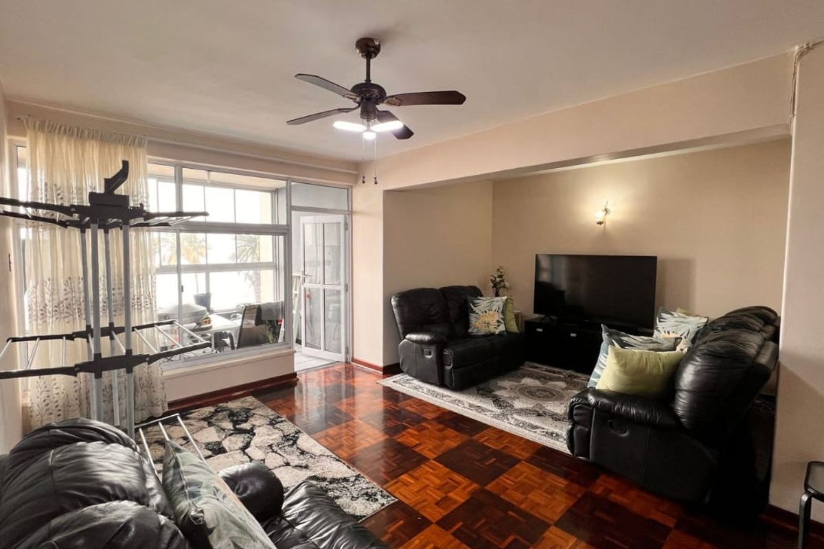 Spacious living area featuring classic parquet flooring, a ceiling fan, and large windows providing natural light and access to an enclosed balcony.