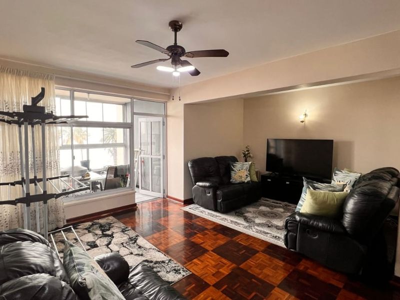 Spacious living area featuring classic parquet flooring, a ceiling fan, and large windows providing natural light and access to an enclosed balcony.