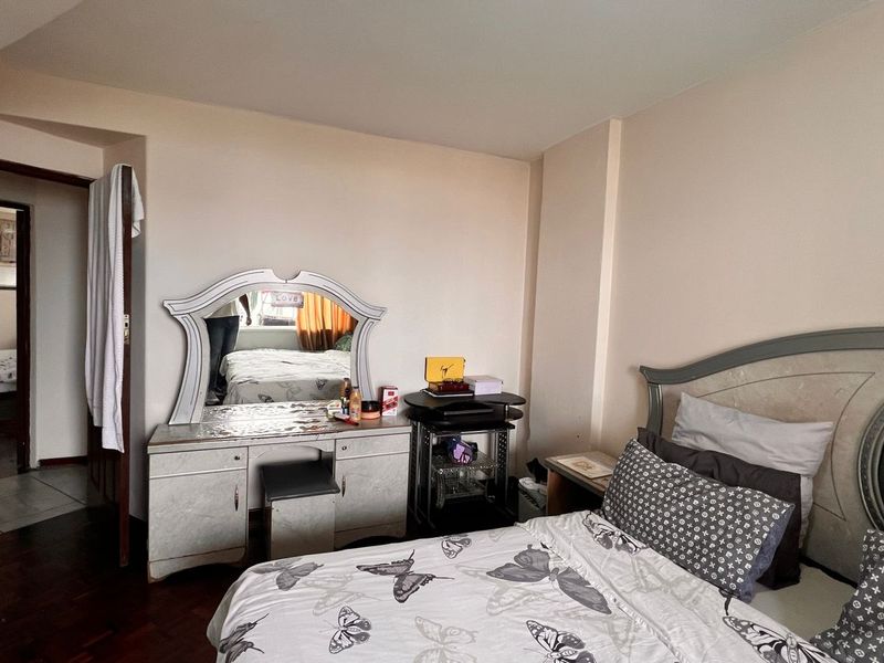 A bedroom featuring dark wood flooring and neutral walls, providing a functional space with access to an adjacent room.