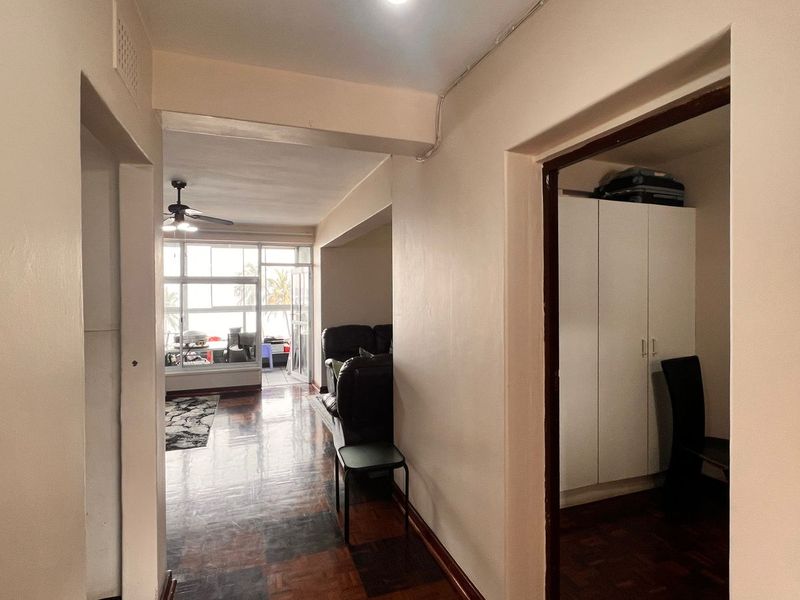 A view from the hallway looking into the living area and an adjacent room, featuring parquet flooring and access to a balcony.