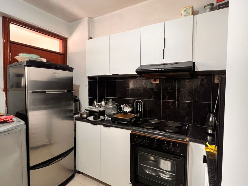 Compact kitchen featuring white cabinetry, black tiled backsplash, and a built-in electric oven with extractor fan.