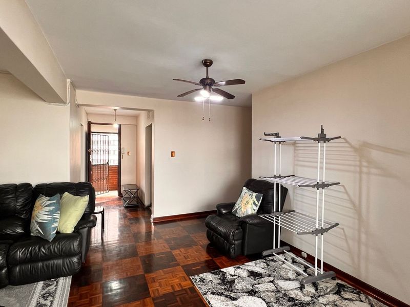 A living room featuring traditional parquet flooring, a ceiling fan, and direct access to an entrance hallway.