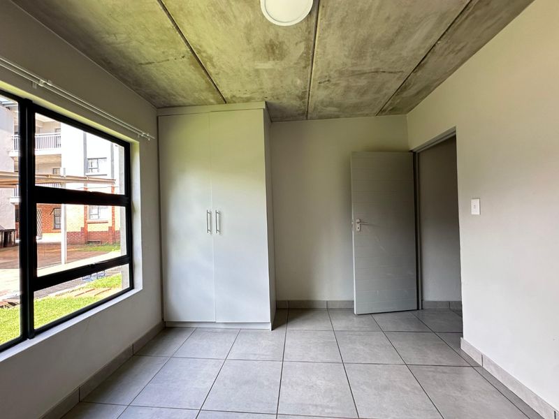 A clean, modern bedroom featuring an exposed concrete ceiling, tiled flooring, and a built-in wardrobe, offering a neutral canvas for personalization.