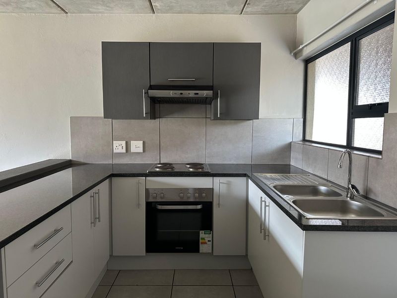 A modern, clean kitchen featuring built-in cabinetry, granite countertops, a stainless steel double sink, and integrated oven with hob and extractor fan.