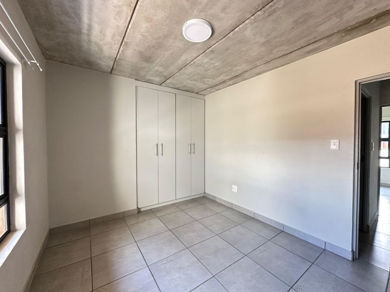 A clean, modern bedroom featuring tiled floors, built-in cupboards, and an exposed concrete ceiling, offering a neutral canvas for personalization.