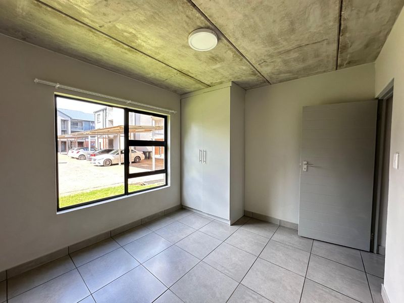 A clean, modern bedroom featuring tiled flooring, an exposed concrete ceiling, and a built-in wardrobe, offering a neutral canvas for personalization.