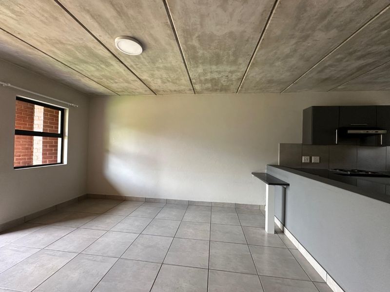 Open plan living and kitchen area featuring modern tiled floors, an exposed concrete ceiling, and a functional breakfast bar.