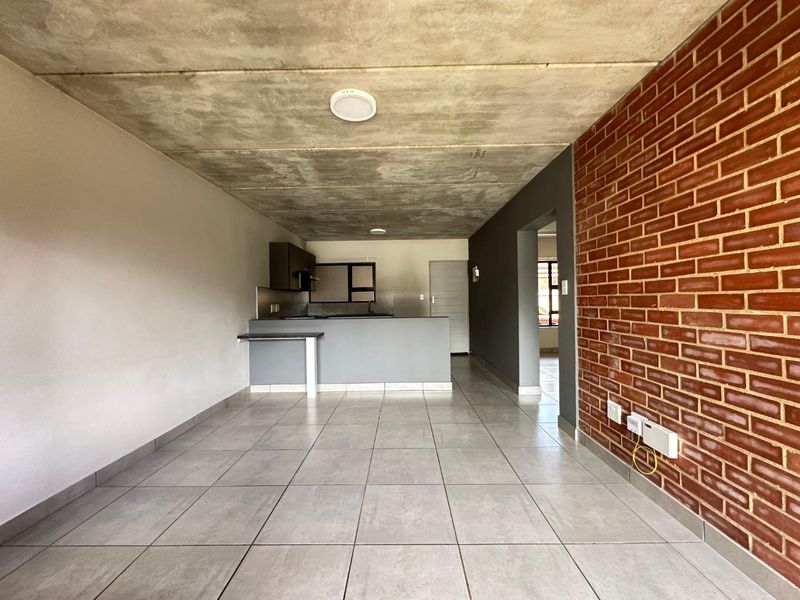 Modern open-plan living area featuring an exposed concrete ceiling, striking brick feature wall, and a functional kitchen with a breakfast bar.