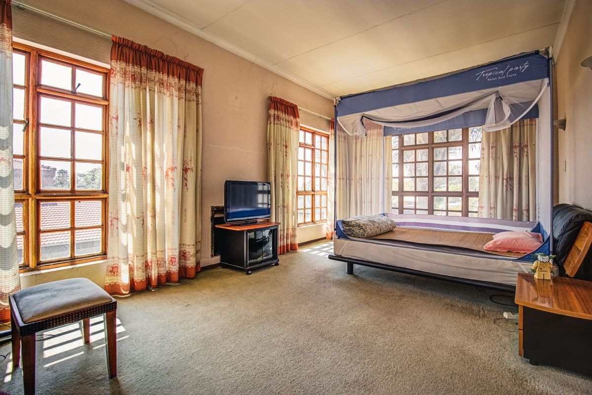 Spacious bedroom featuring large timber-framed windows, carpeted flooring, and classic cornicing, offering a bright and airy atmosphere with potential for modernization.