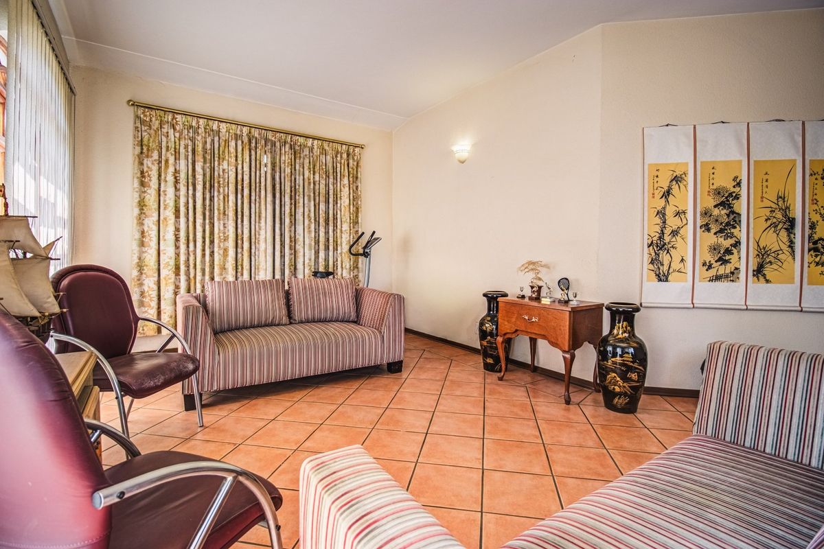 A living room featuring terracotta floor tiles, neutral walls, and a large window with curtain treatments.