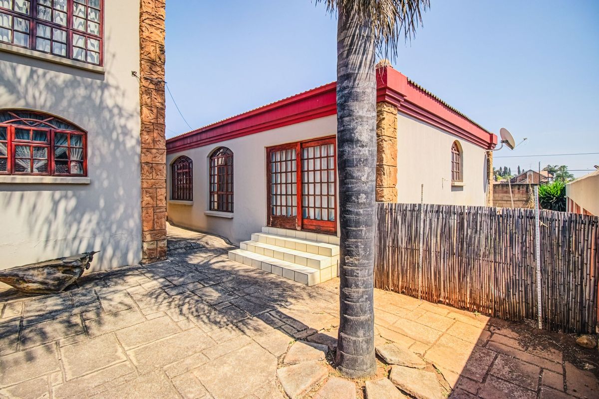 Rear exterior view of the property featuring a paved patio area, stone-clad accents, arched windows, and timber-framed glass doors leading into the home.