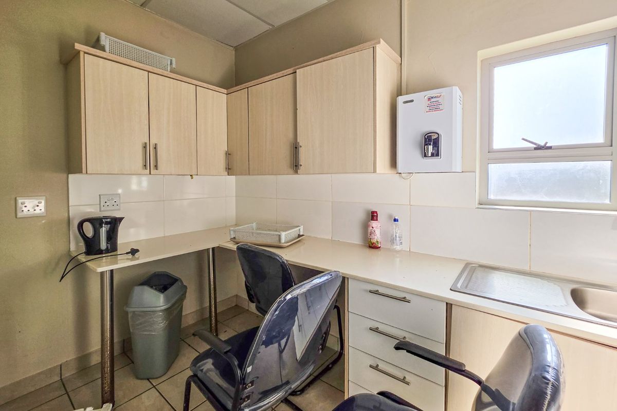 A functional kitchenette featuring laminate cabinetry, tiled backsplash, stainless steel sink, and a wall-mounted water dispenser in a commercial office setting.