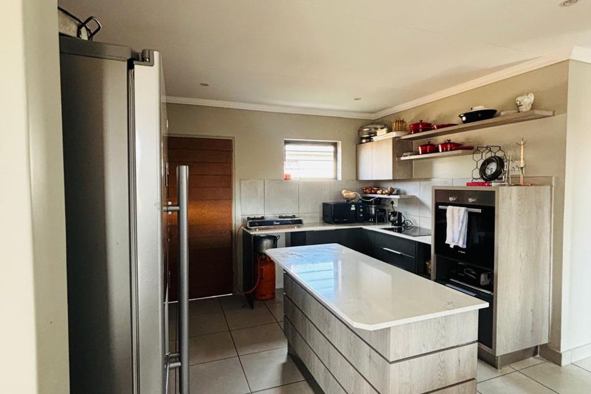 Modern kitchen featuring a central island, built-in oven, hob, and sleek cabinetry with floating shelving, finished with neutral floor tiles.