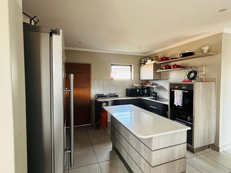 Modern kitchen featuring a central island, built-in oven, hob, and sleek cabinetry with floating shelving, finished with neutral floor tiles.