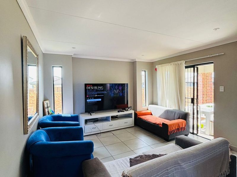 A well-lit living room featuring neutral tiled flooring, recessed ceiling lights, and a sliding glass door providing access to the outdoor area.