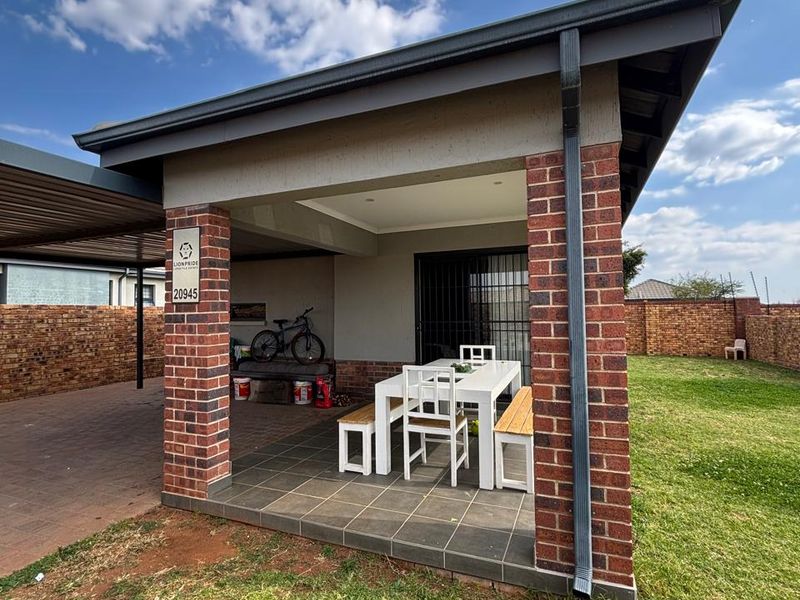 A covered outdoor patio area featuring brick pillars, tiled flooring, and integrated downlights, overlooking a private garden and paved driveway.