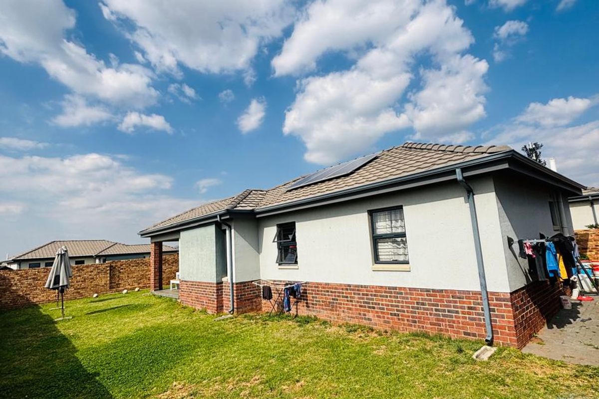 Rear view of the house featuring a brick and plaster facade, tiled roof with solar panels, and a private garden area with boundary wall.