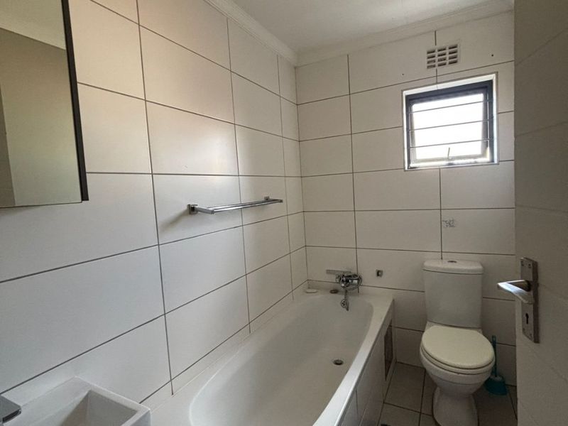 A clean, functional bathroom featuring white wall tiles, a built-in bathtub, a wall-mounted basin, and a standard toilet.