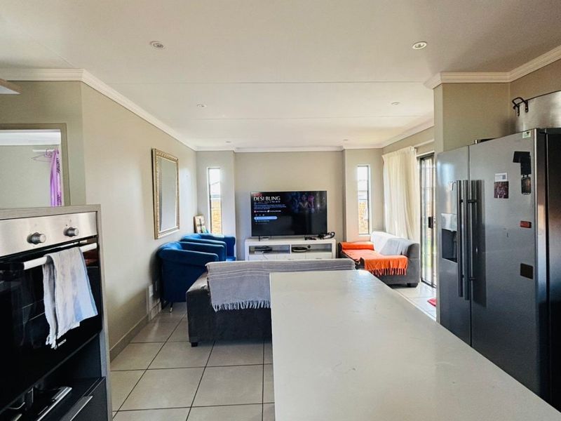 Open-plan living area featuring a central kitchen island, built-in oven, and tiled flooring, seamlessly connecting the kitchen to the lounge space.