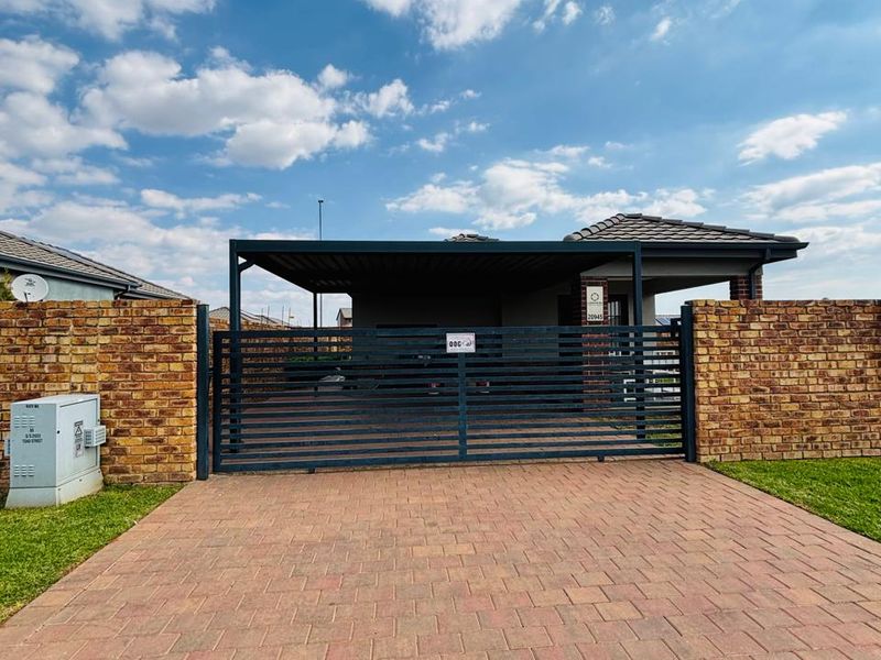 Front view of the property featuring a paved driveway, secure metal sliding gate, brick boundary walls, and a covered carport.