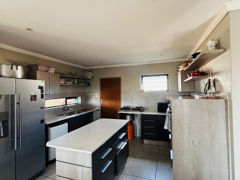 Modern kitchen featuring a central island, stone countertops, dark cabinetry, tiled flooring, and recessed lighting, offering a functional and contemporary cooking space.