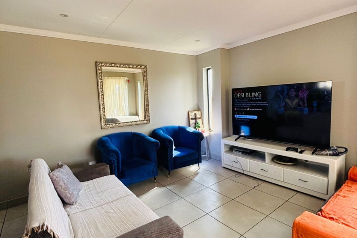 A comfortable living room featuring neutral wall tones, large format floor tiles, and recessed ceiling lighting, providing a functional and well-lit space.