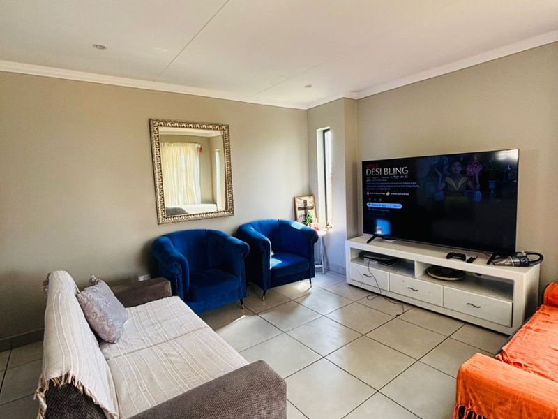 A comfortable living room featuring neutral wall tones, large format floor tiles, and recessed ceiling lighting, providing a functional and well-lit space.
