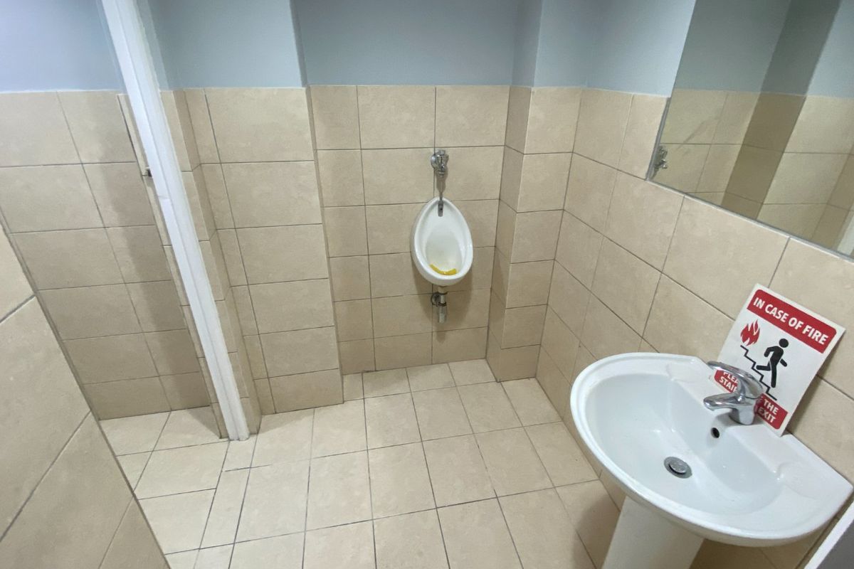 A commercial restroom facility featuring a wall-mounted urinal, pedestal sink, and tiled wall and floor finishes.